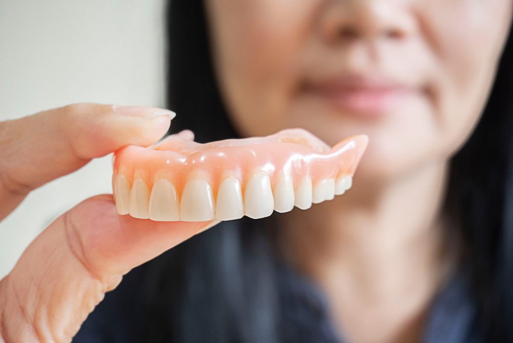 Happy asian woman be smile and holding dentures in hand. Happy asian woman be smile and holding dentures in hand. Dentures for prosthetic devices constructed to replace missing teeth and helping to chew food.