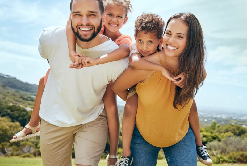 Happy family, mother and father with children on back in a nature park for bonding and relaxing in summer. Smile, mom an dad love enjoying quality time with siblings or kids outdoors for fresh air