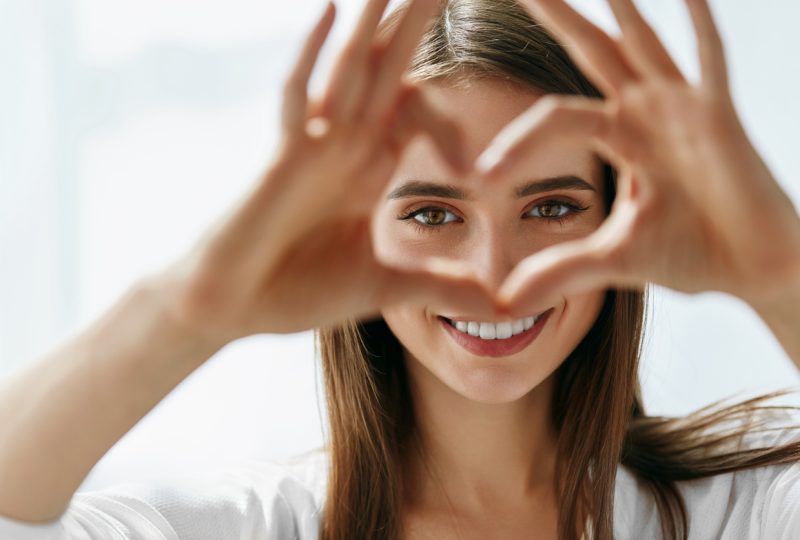 Healthy Eyes And Vision. Portrait Of Beautiful Happy Woman Holding Heart Shaped Hands Near Eyes. Closeup Of Smiling Girl With Healthy Skin Showing Love Sign. Eyecare. High Resolution Image
